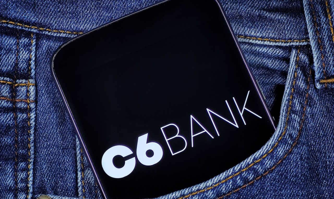 Celular com a logo do c6 bank no bolso de uma calça.