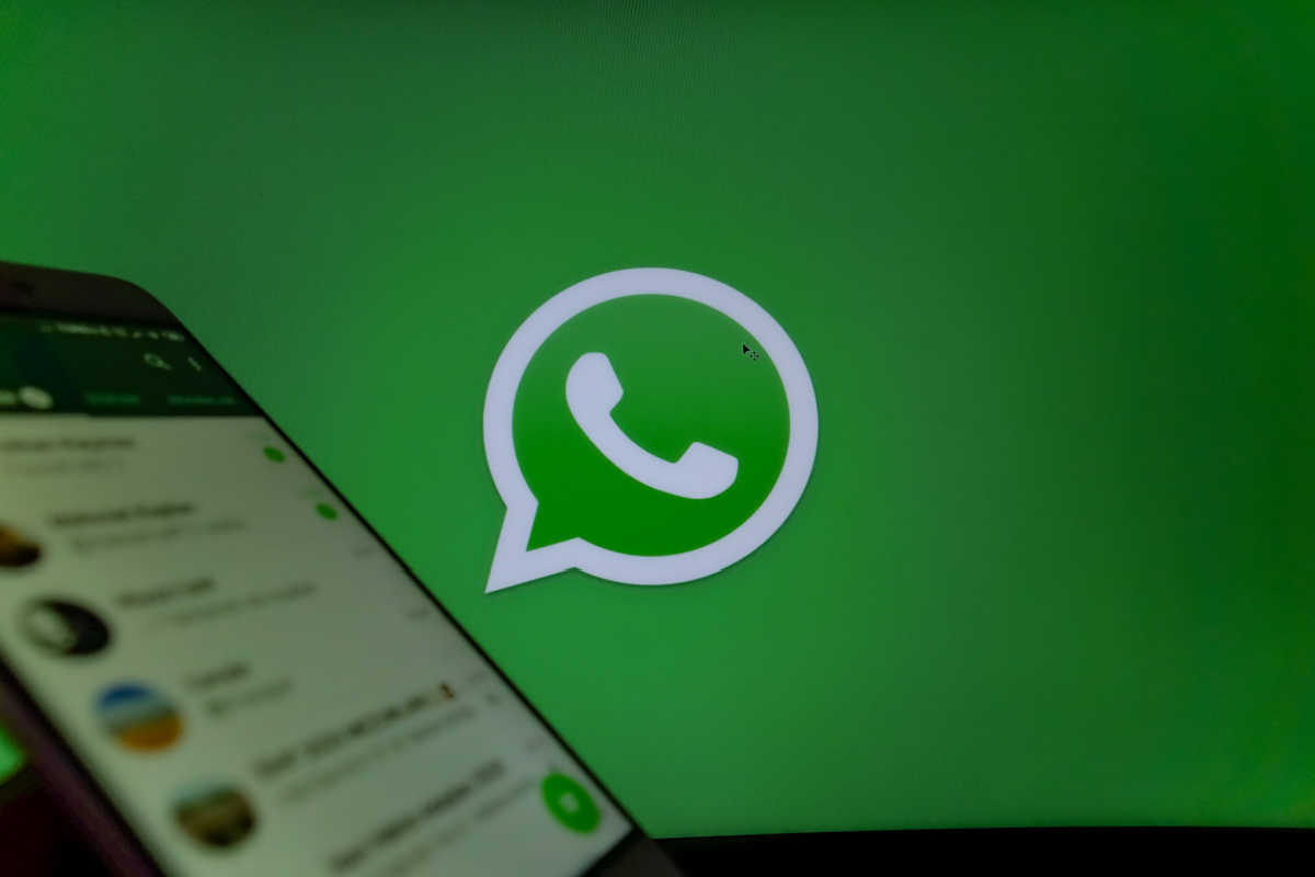 celular com WhatsApp aberto e um fundo verde com o logo do app atrás.