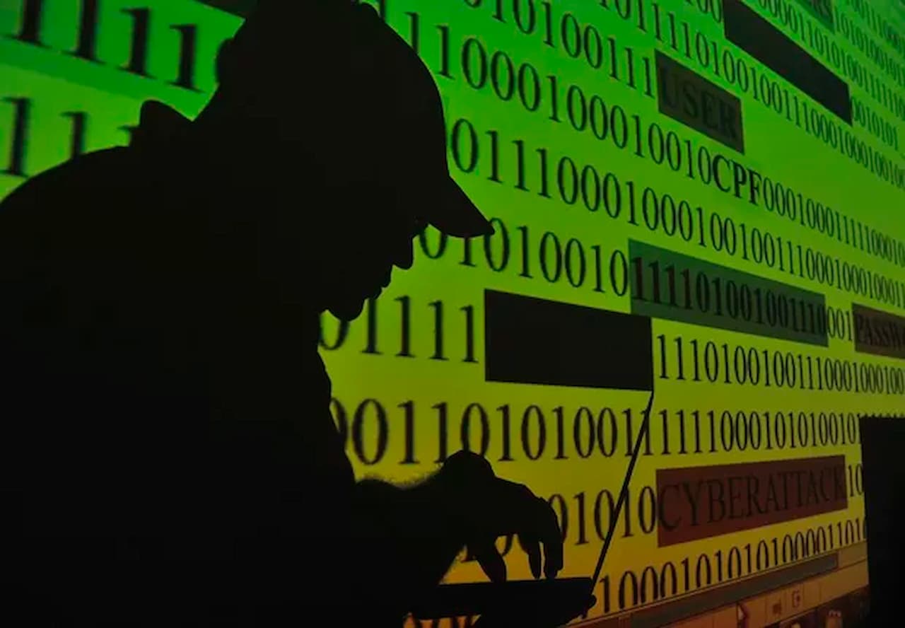 Sombra de hacker virtual mexendo em notebook e código binário ao fundo