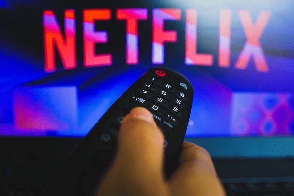 Mão segurando controle em frente a uma televisão que está com o logo da Netflix
