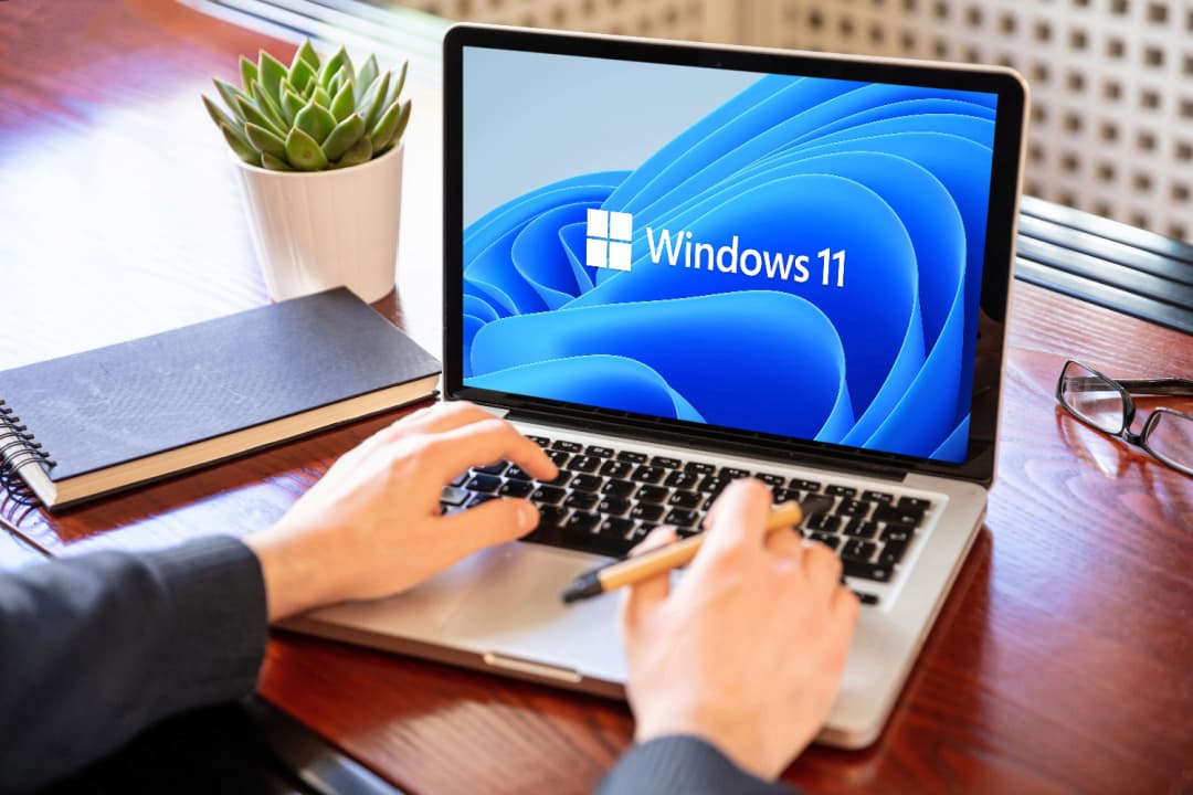 Pessoa mexendo em um notebook cuja tela mostra a tela de início do Windows 11