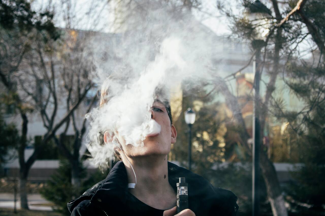Homem fumando cigarro eletrônico e com fumaça na frente do rosto