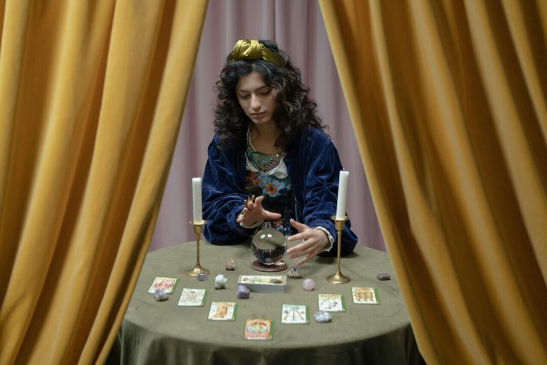 Mulher sentada atrás de uma mesa com bola de cristal, velas e cartas de tarô